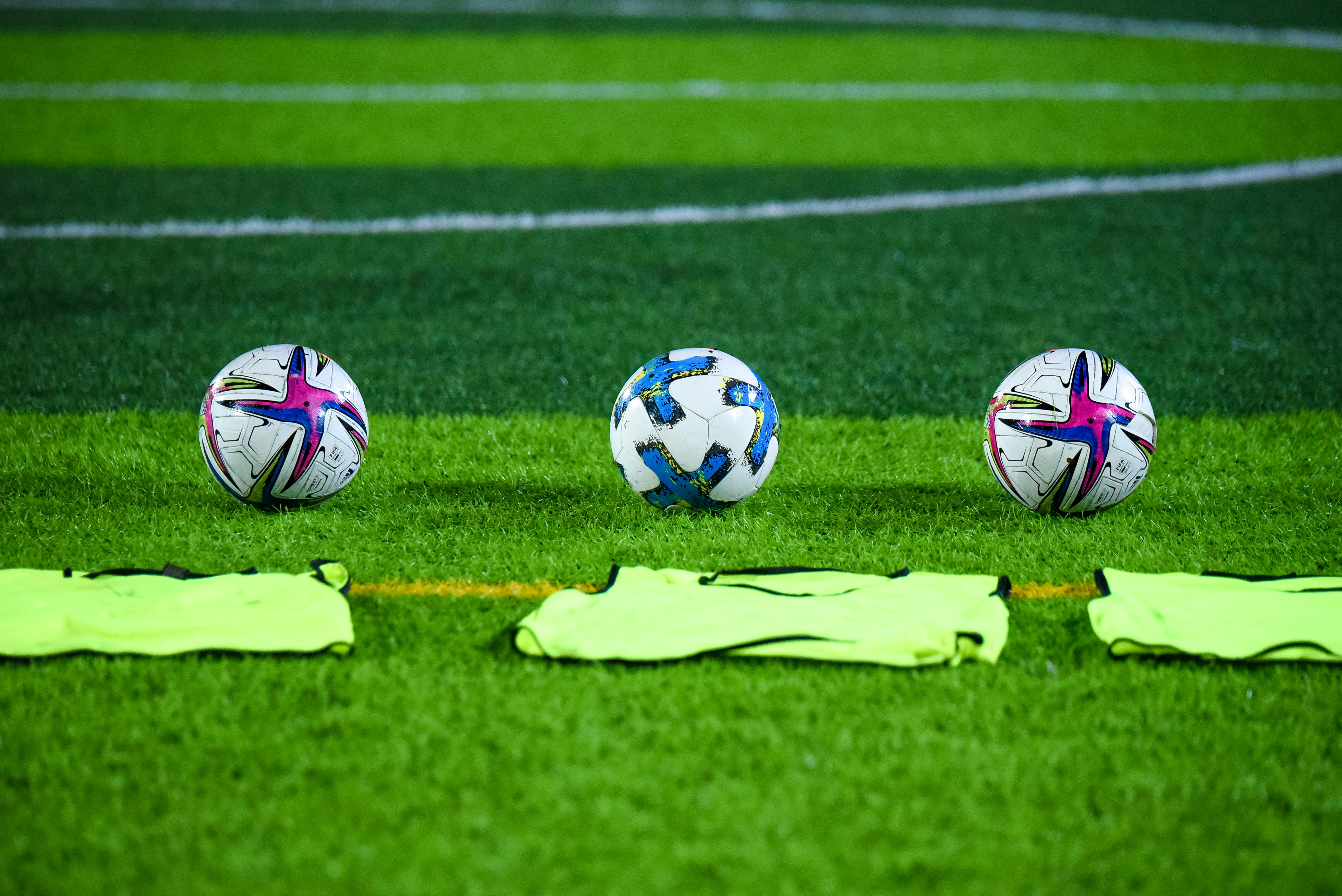 Three soccer balls and training bibs on a lush green field.